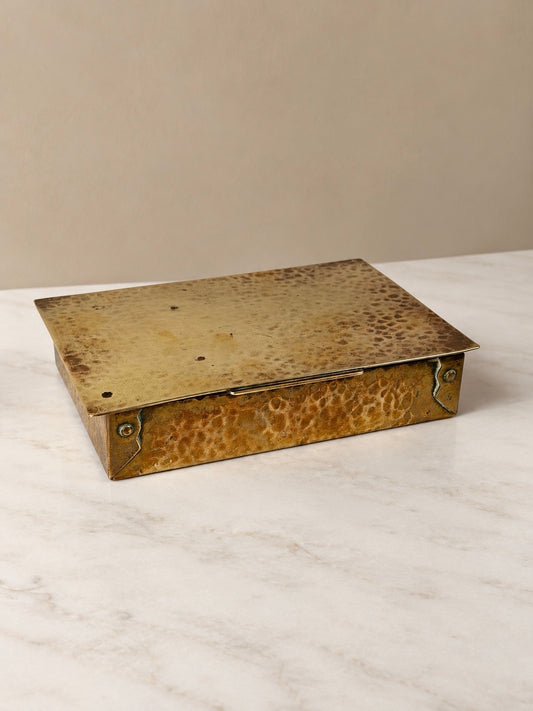 Rectangular hammered brass lidded box with decorative metal corner fittings, hinged lid and cork-lined interior.