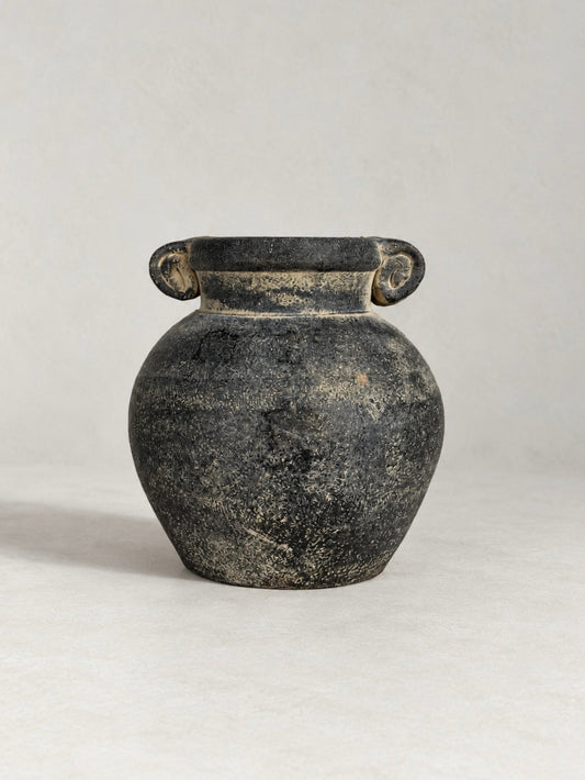 Black ceramic urn with a rounded body, twin scroll handles and a heavily textured, distressed finish with contrasting pale tones.